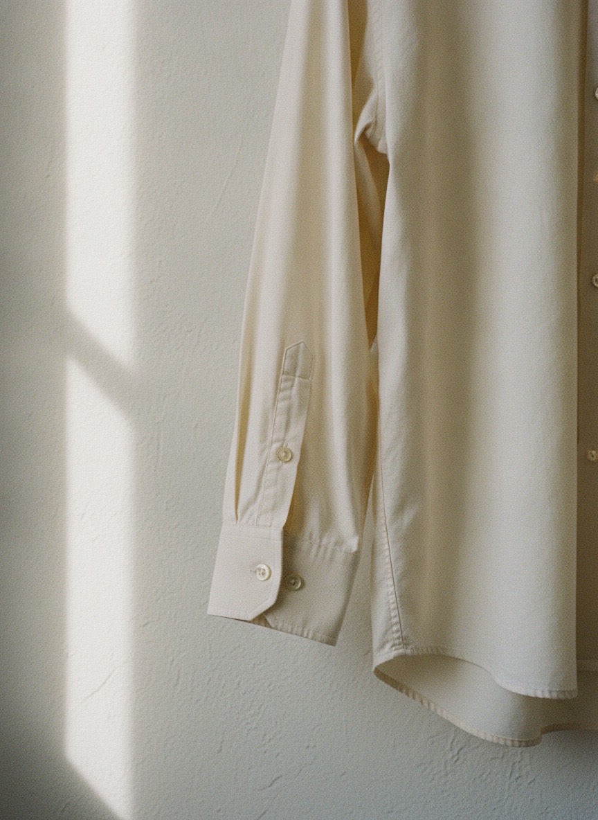 An unbranded cream shirt sleeve and cuff detail against a plaster wall.